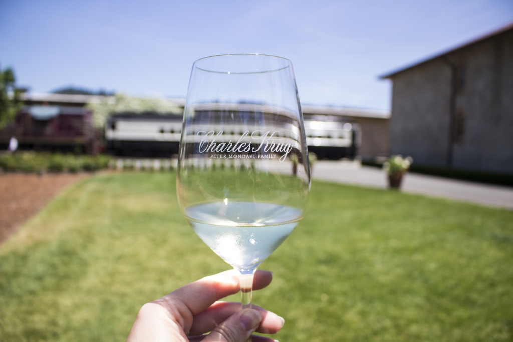 A hand holds a glass of California white wine from Charles Krug up to the sky.