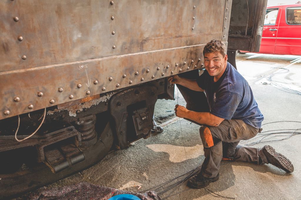 A restoration worker kneels outside an antique railcar that is being refurbished. 