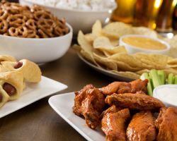 Party snacks: Hot wings, pig in the blankets, pretzels, nacho chips and popcorn displayed on white plates on a dark wood table