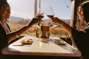 Two people sit at a table onboard the Napa Valley Wine Train. They each hold a glass of red wine, clicking their glasses together over their table.