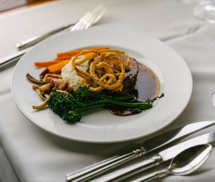 Professionally plated Steak, mashed potatoes, broccoli, crisp onions, and carrots