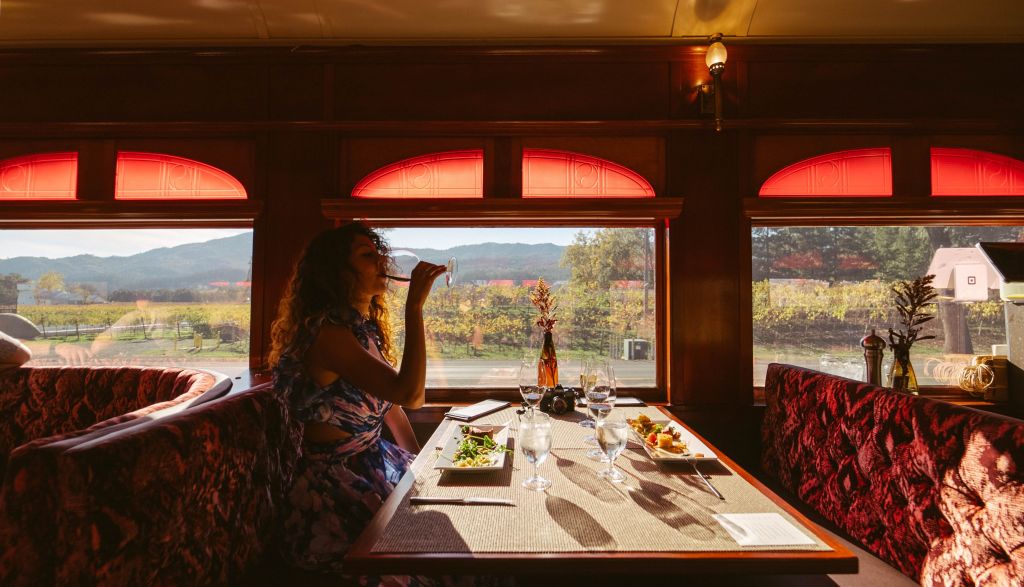 Woman drinking from her wine glass, sat in an elegant red booth