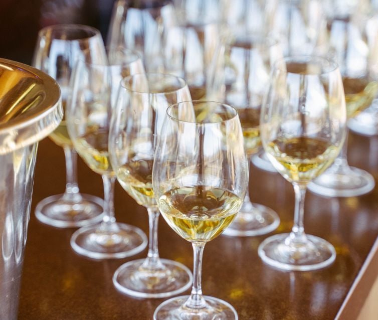 Several rows of wine glasses lined up with white wine in them.