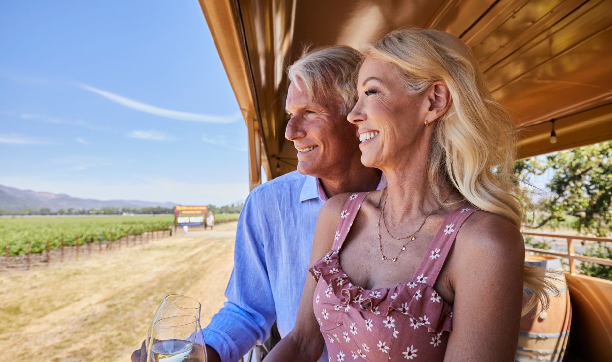 A man and woman smile and look onward from an open window towards a vineyard.
