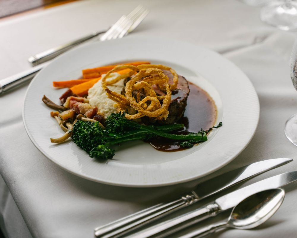Professionally plated Steak, mashed potatoes, broccoli, crisp onions, and carrots