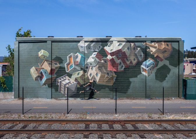 A woman jumps in front of an mural wall
