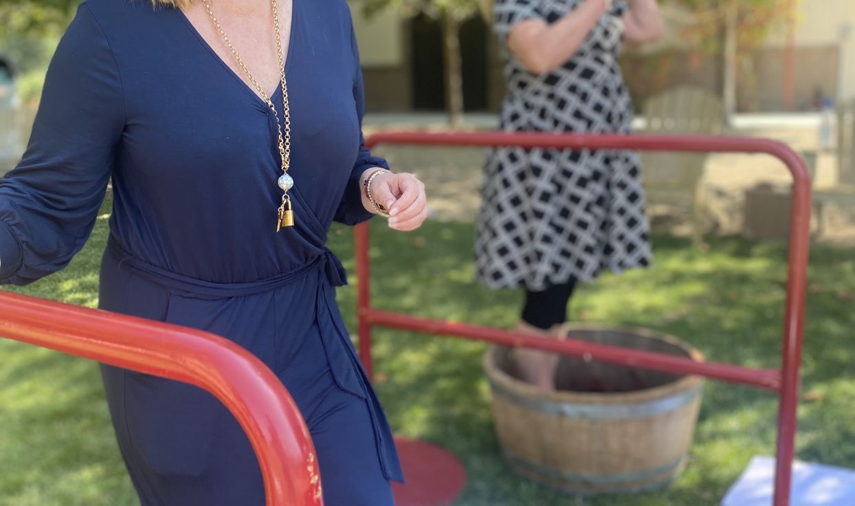 Two adults stand in wine barrels mashing grapes with their feet